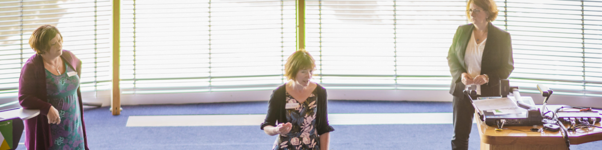Kate Flory coaching at the front of a large room.